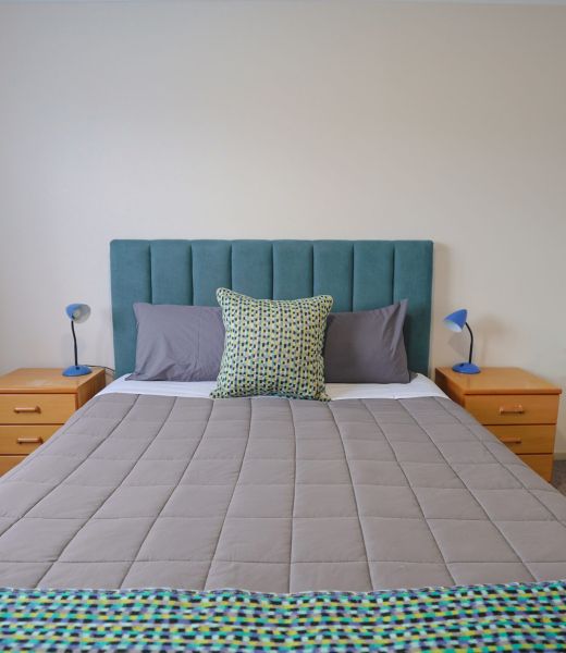Queen bed with a teal upholstered headboard and bedside lamps at Fitzgerald on King